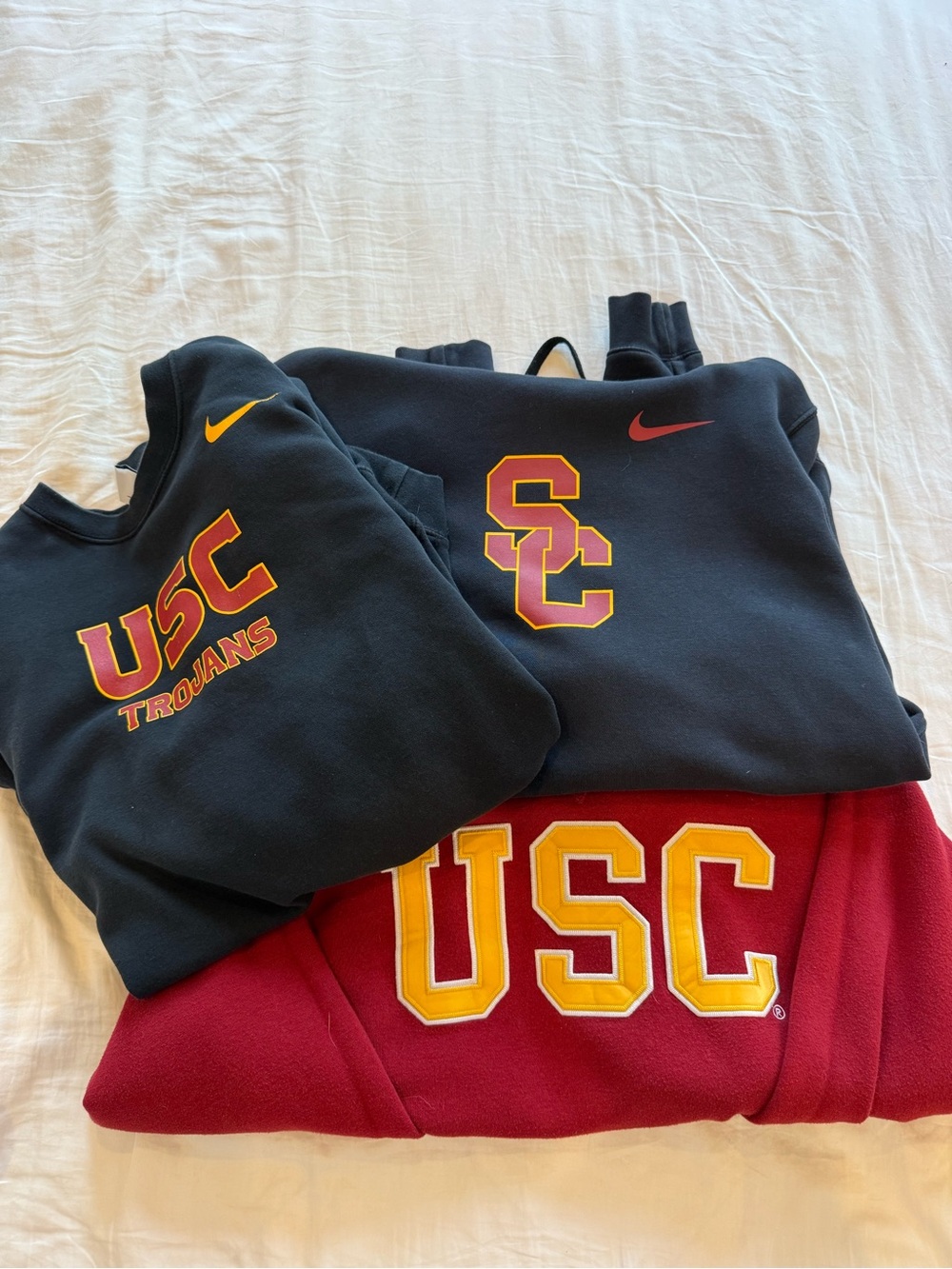 USC red crewneck, black Nike crewneck, and black Nike hoodie